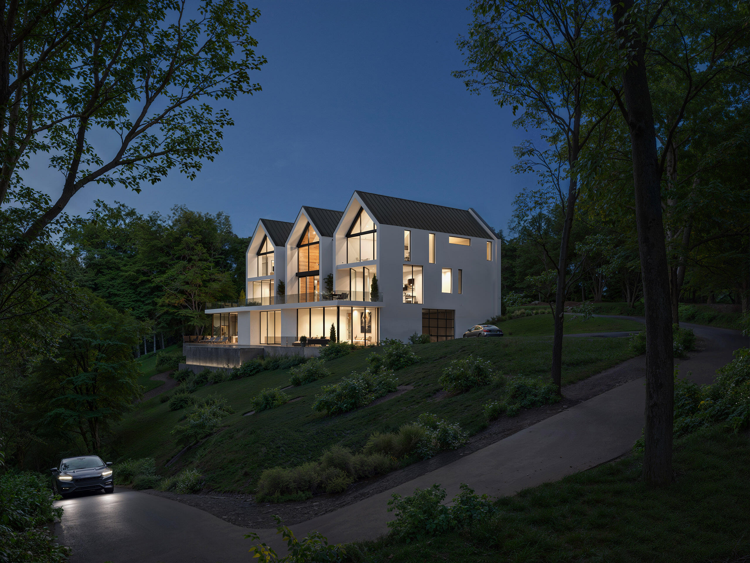 Modern multi-level house built on slope with warm lighting – evening render